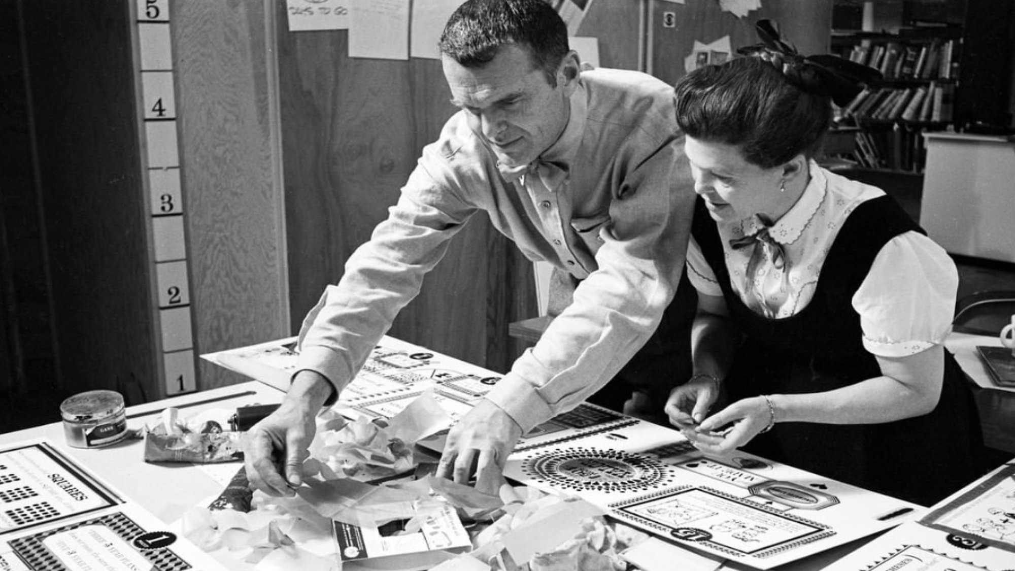 Ray & Charles Eames standing at a table working.
