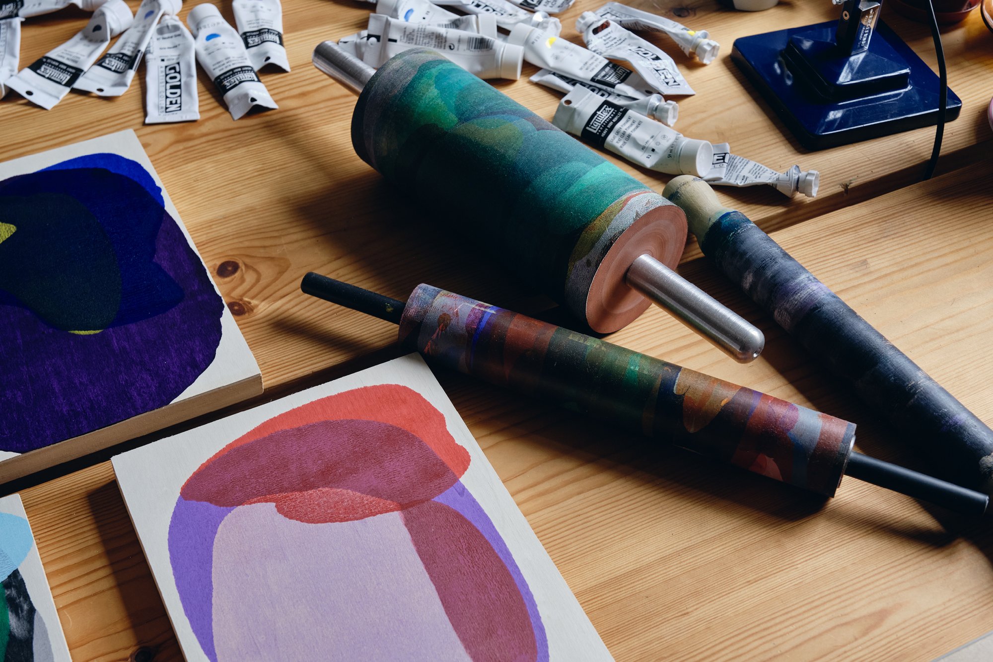 Artist Daniel Eatock’s work table in his London art studio featuring various rolling pin paintings, rolling pins, and paints.