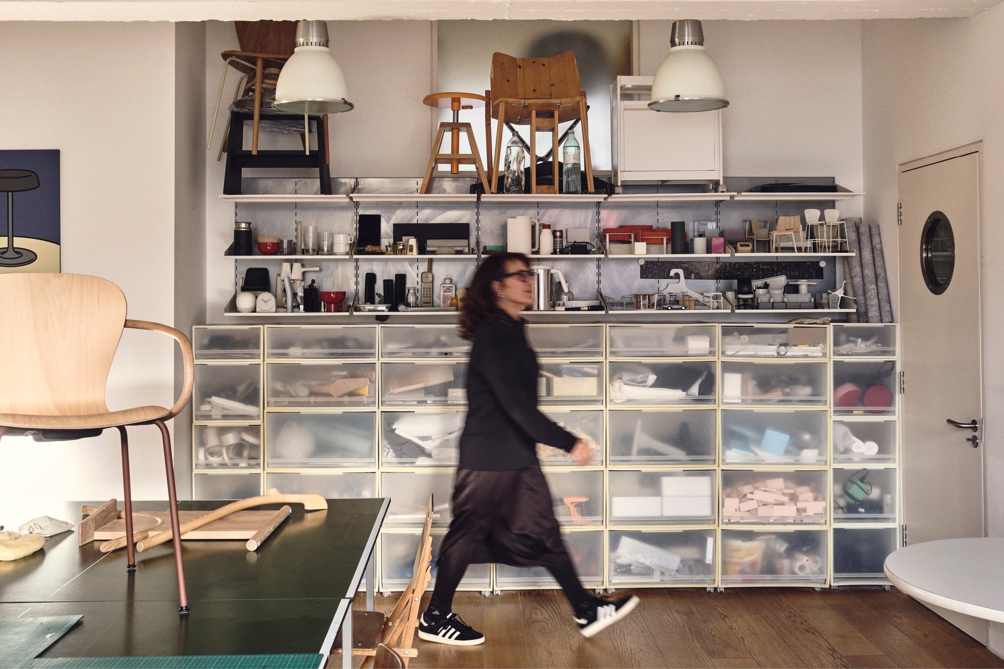Kim Colin of design studio Industrial Facility walking past shelves with many objects and prototypes designed by the firm.