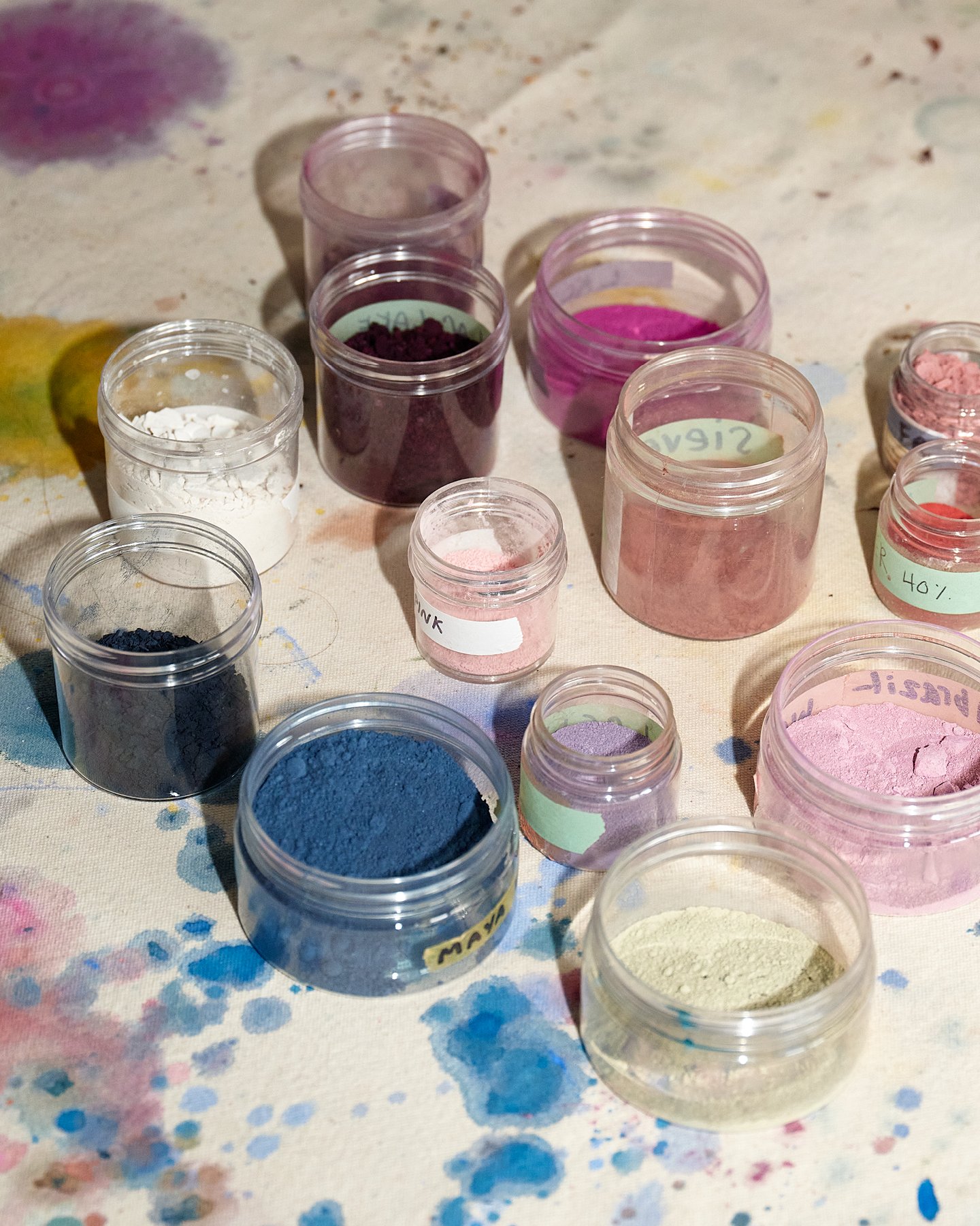 Jars of many richly colored pigments made by abstract artist Natalie Stopka displayed on a pigment stained work surface.
