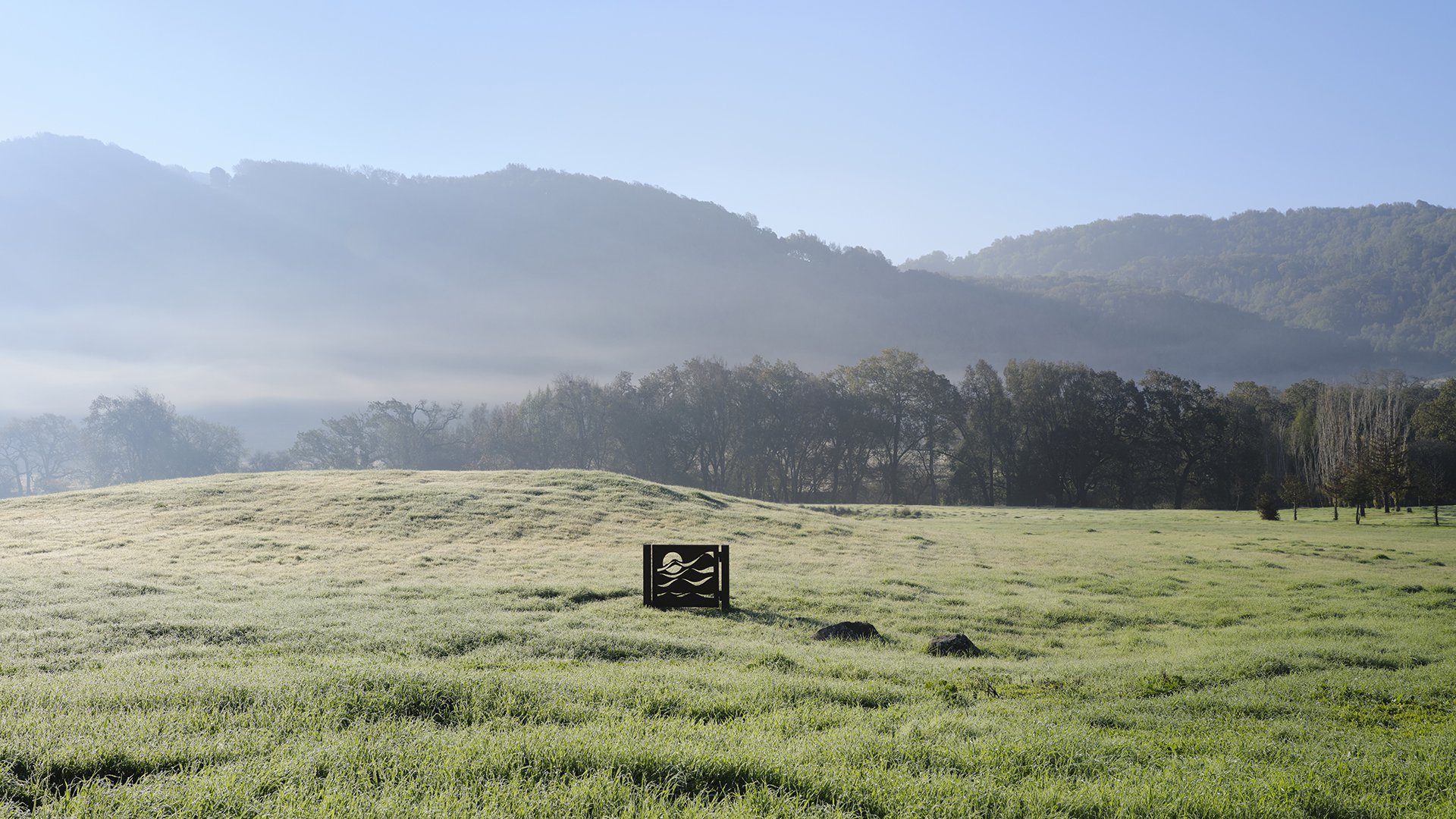 Eames Institute Ranch property with rolling hills in the background, and a large grass field featuring a metal sculpture designed by Lucia Eames.