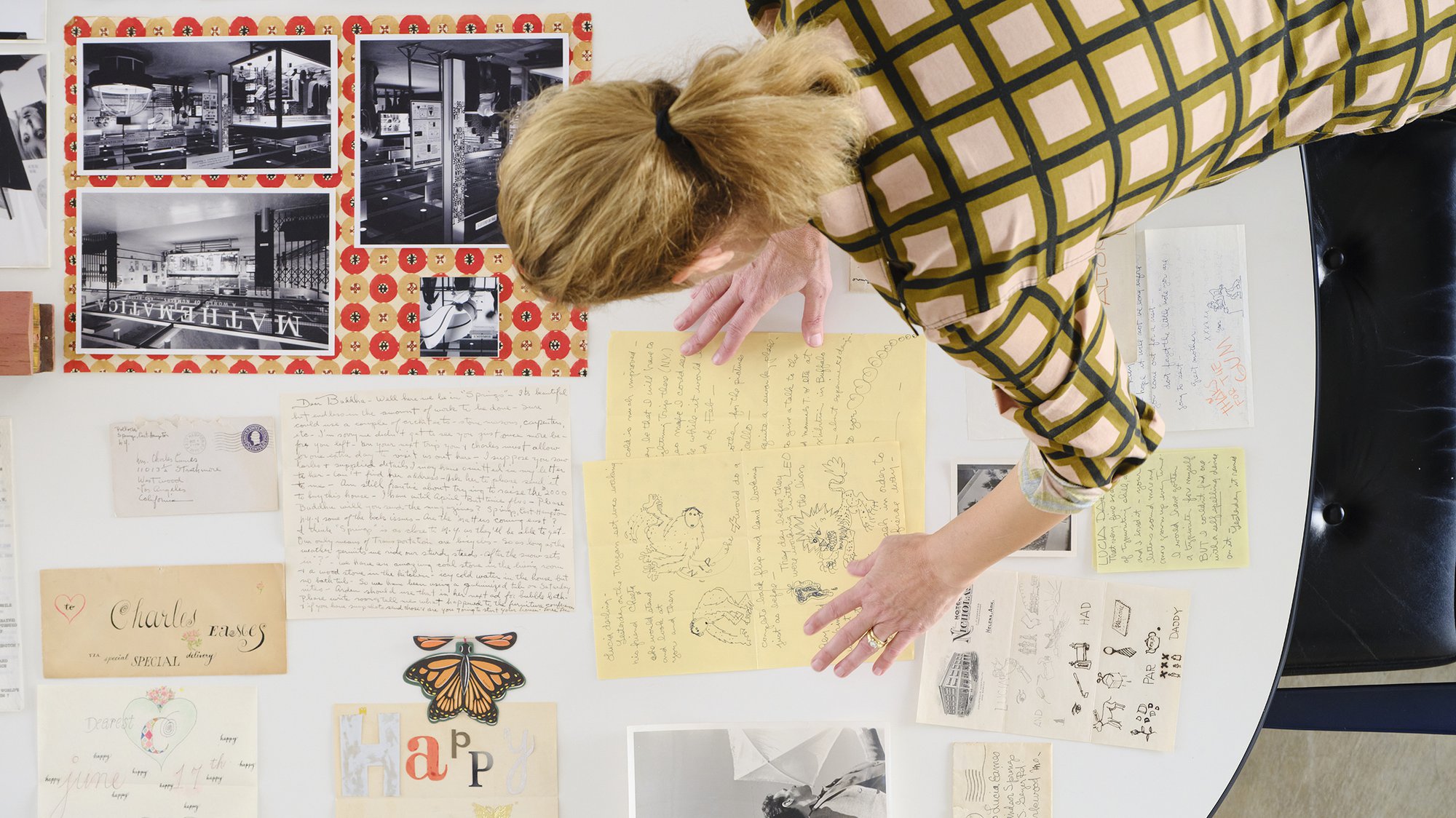 Top down view of Llisa Demetrios standing over a table with various Eames writings and sketches.