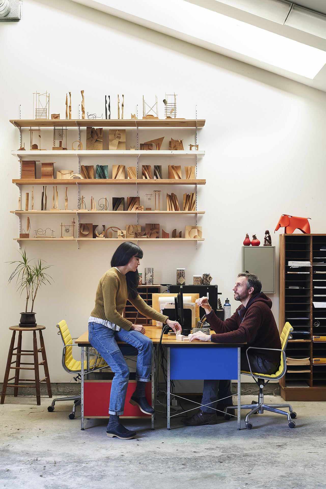 Interior of the Eames Ranch with employees at a table and shelves in the background with models of sculptures made by Llisa Demetrios, Granddaughter of Charles Eames.