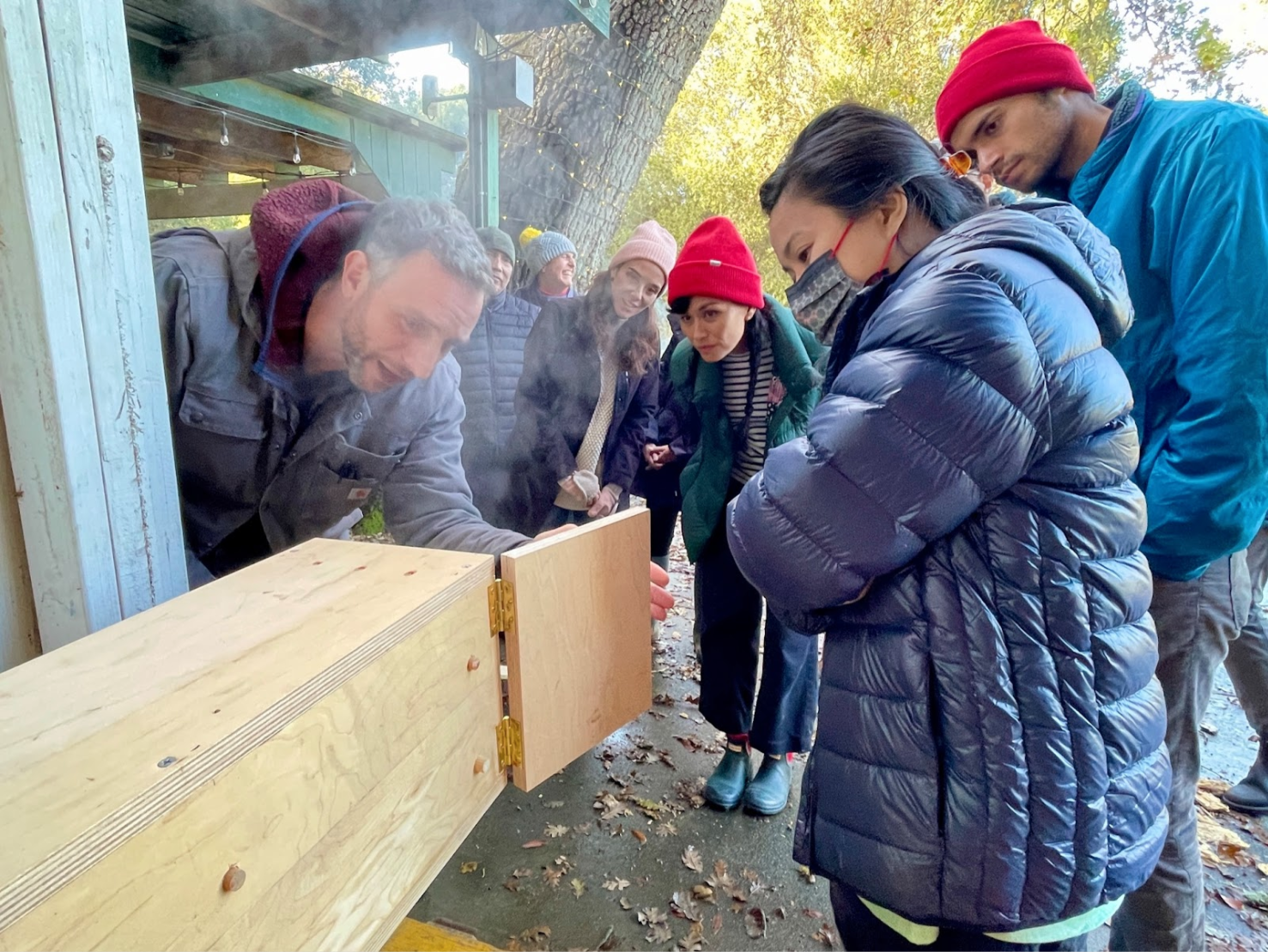 Eames Institute employees gathered outside of the Eames Ranch around a prototype used to bend wood.