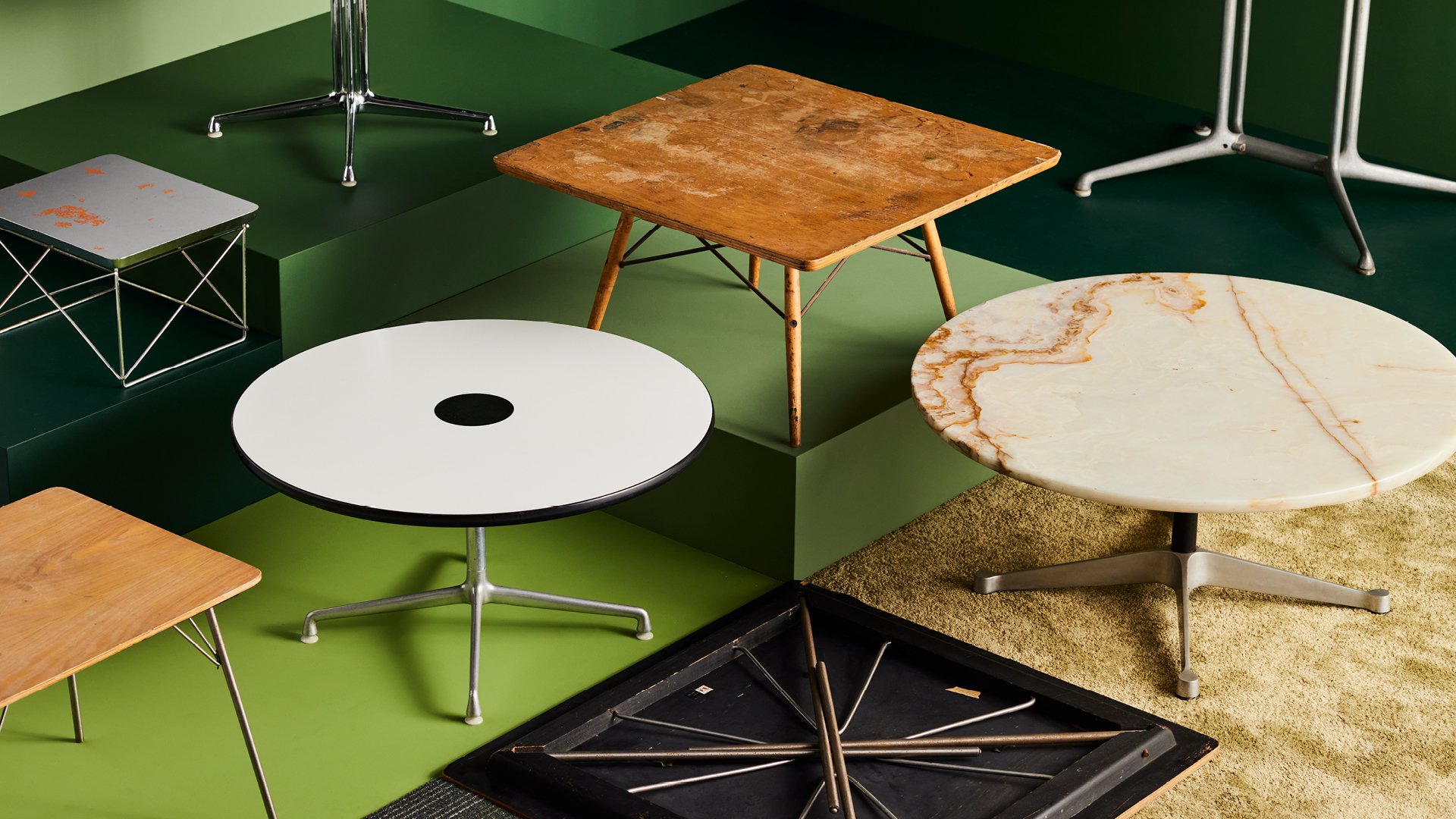 Several Eames tables made of various materials displayed on colorful pedestals.